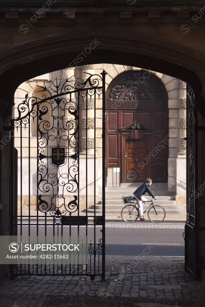 England, Oxfordshire, Oxford. A cyclist travelling along the High Street past a gateway at the end of Logic Lane named after the location of a school of logicians.