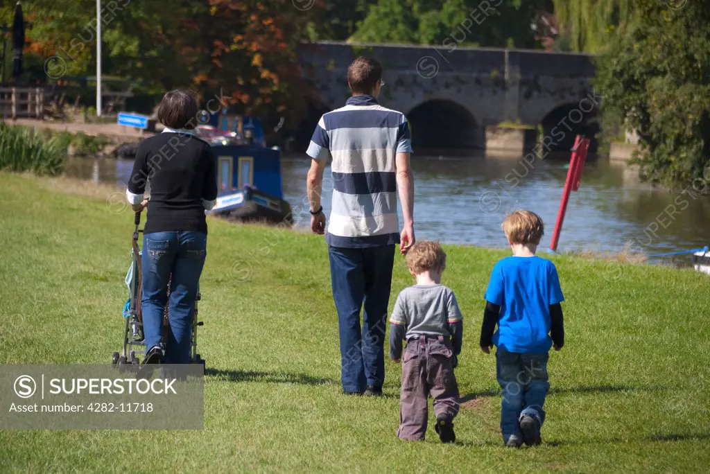 England, Oxfordshire, Abingdon. A young family walking along the riverbank of the River Thames towards Abingdon Bridge.