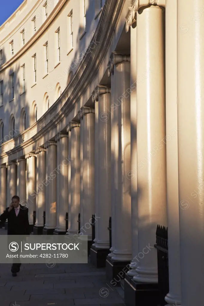 England, London, Regent's Park Crescent. A man wearing a suit walking past stuccoed terraced houses on Park Crescent whilst talking on his mobile phone.