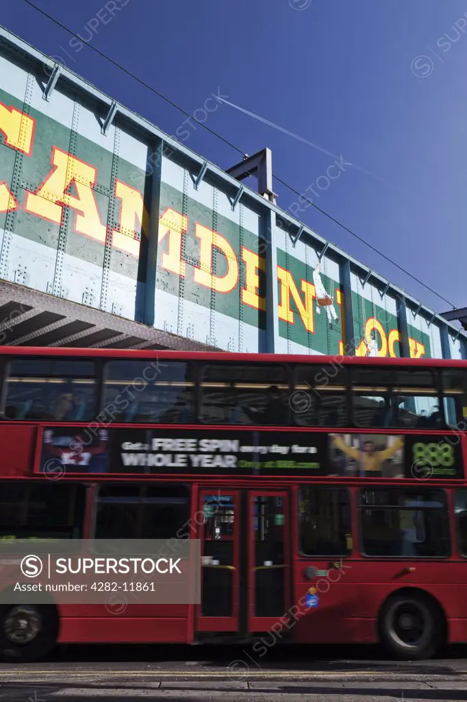 England, London, Camden. A red double decker bus passing under the old railway bridge over Chalk Farm Road at Camden Lock. The bridge features a 'trompe l'oeil' image which has become the icon for Camden Lock.