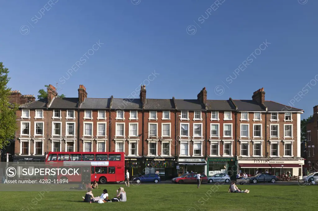 England, London, Blackheath. People relaxing on the heath opposite a parade of shops and restaurants.