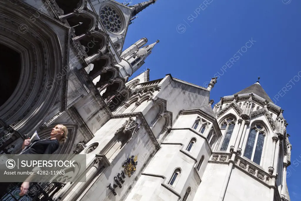 England, London, The Strand. A young woman walking past the Royal Courts of Justice carrying legal papers.