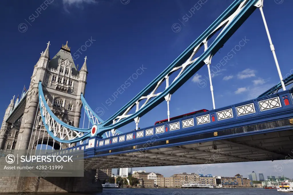 England, London, Tower Bridge. A red London bus crossing the River Thames over Tower Bridge, one of London's most famous and iconic landmarks.