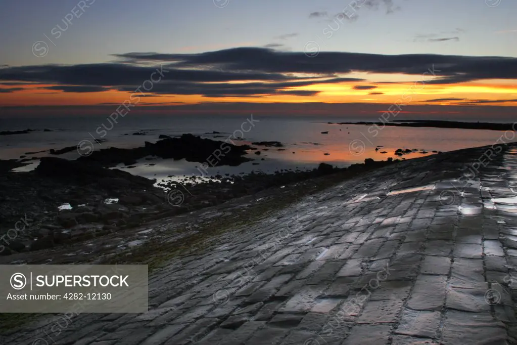 England, North Tyneside, Cullercoats. A colourful sunrise reflects in the still waters of the North Sea.