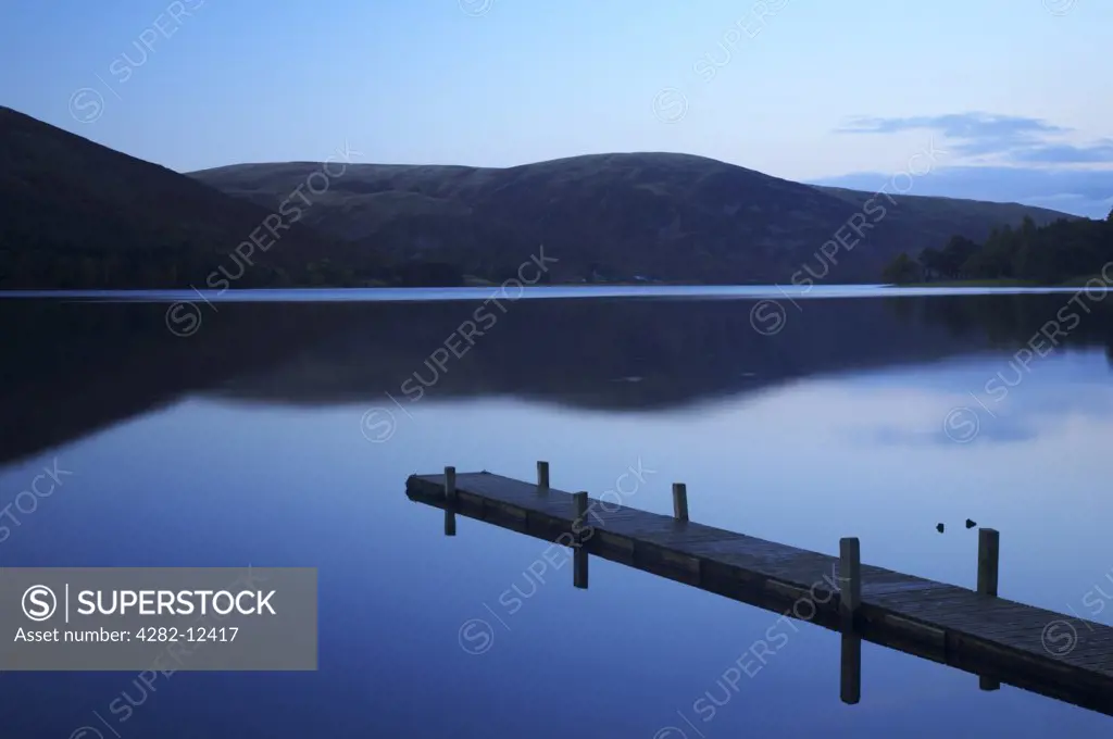 Scotland, Scottish Borders, St Marys Loch. St Marys Loch at dusk, with the surrounding hills and lakeside jetty reflected in the still waters of the loch.