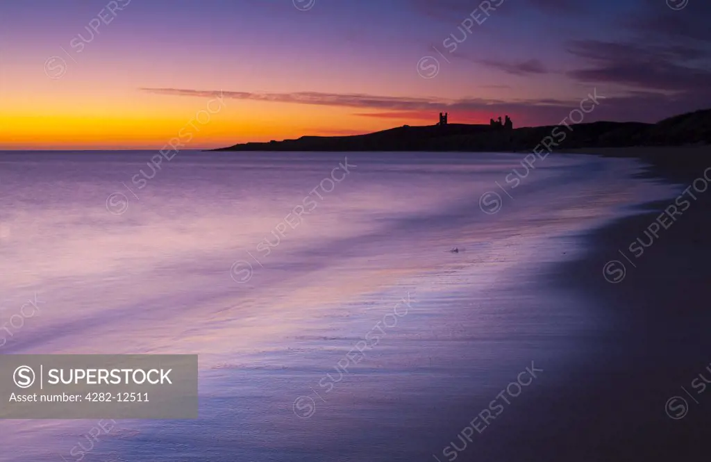 England, Northumberland, Embleton Bay. A colourful display of pre-dawn colours relected upon the wet sands of Embleton Bay, overlooked by the dramatic ruins of Dunstanburgh Castle.