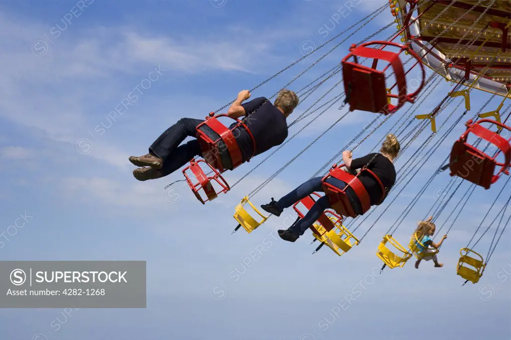 England, Kent, Whitstable. People enjoying a ride on a traditional Chair-o-plane carousel at a fair in Whitstable.