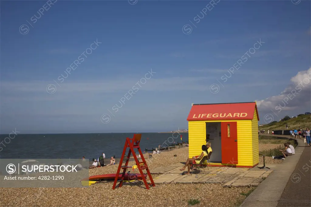 England, Kent, Whitstable. Two lifeguards sitting on duty outside their hut on the beach at Whitstable.