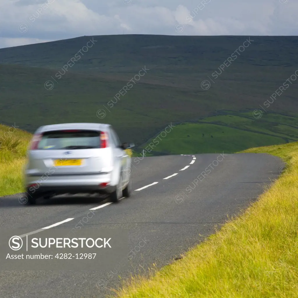 England, Northumberland, North Pennines. A car travelling along a country road running through dramatic Pennine scenery, in the North Pennines Area of Outstanding Beauty.