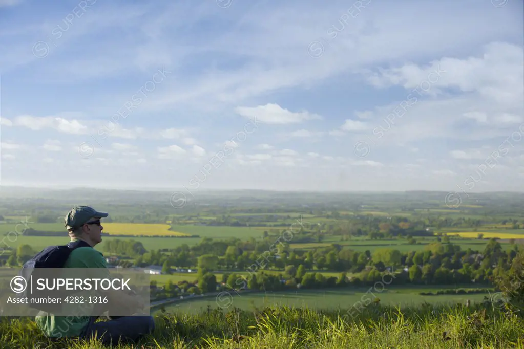 England, Buckinghamshire, Stokenchurch. A man carrying a rucksack on his back sitting on a hill looking out over the landscape below.