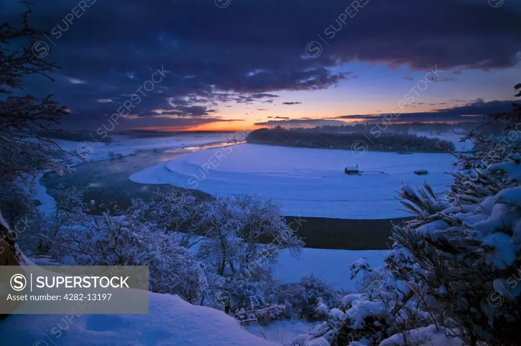 Scotland, Scottish Borders, Ladykirk. A winter landscape featuring the River Tweed at Norham Dene and The Sands Shiel across the river and border on the Scottish side at sunset during the winter of 2010.