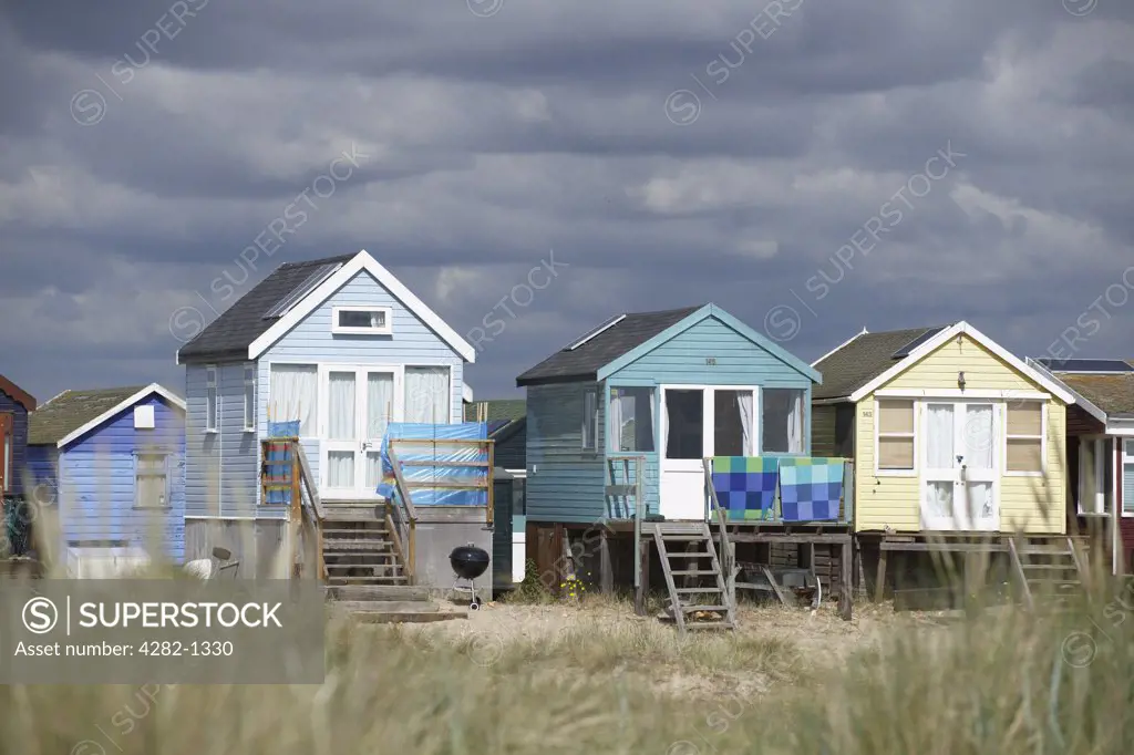 England, Dorset, Mudeford. A view through long grass towards beach huts on the seafront at Mudeford, two miles from Christchurch.