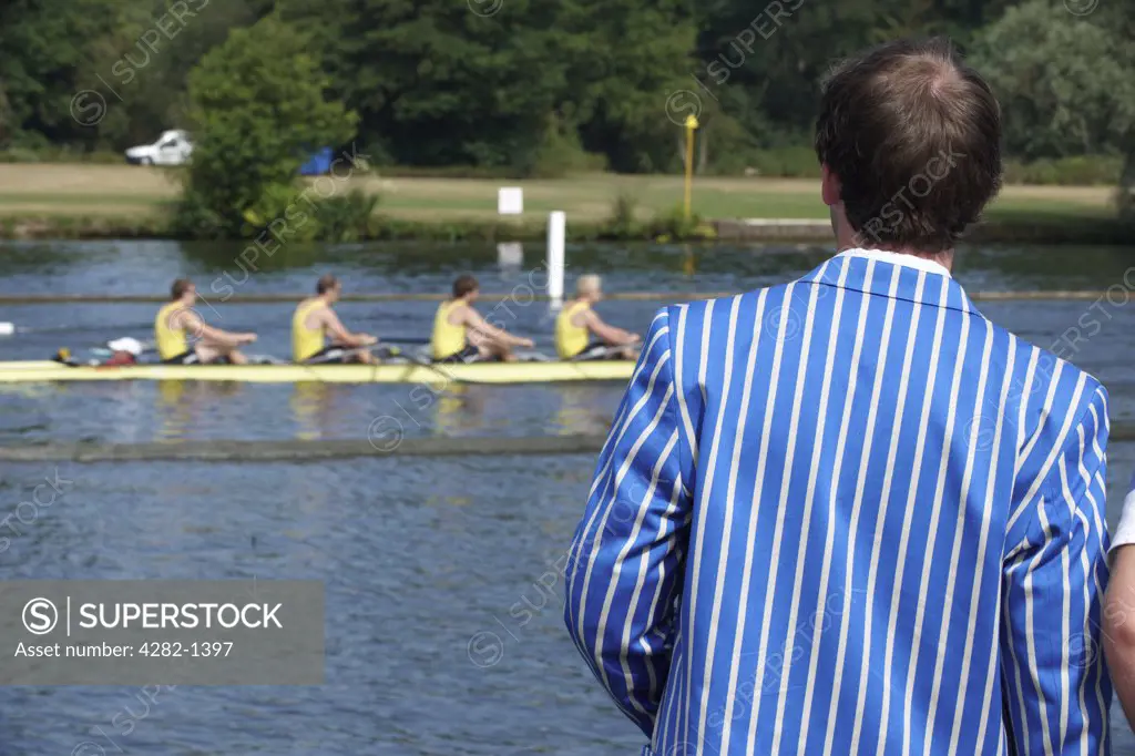 England, Oxfordshire, Henley-on-Thames. A spectator wearing a rowing club blazer watching a race from the riverside at the annual Henley Royal Regatta.
