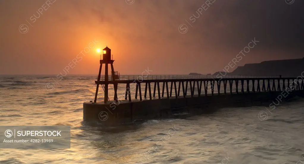 England, North Yorkshire, Whitby. Sunrise behind Whitby East Pier Light (New).