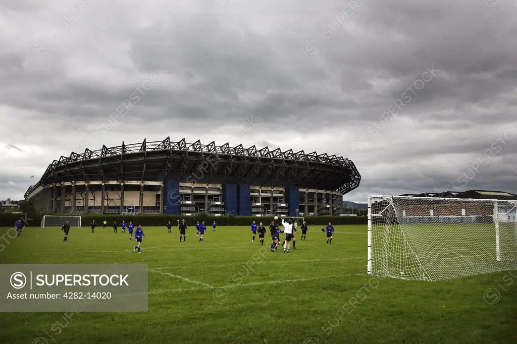 Scotland, Midlothian, Edinburgh. A football game in Roseburn Park with Murrayfield Rugby Stadium providing the backdrop.