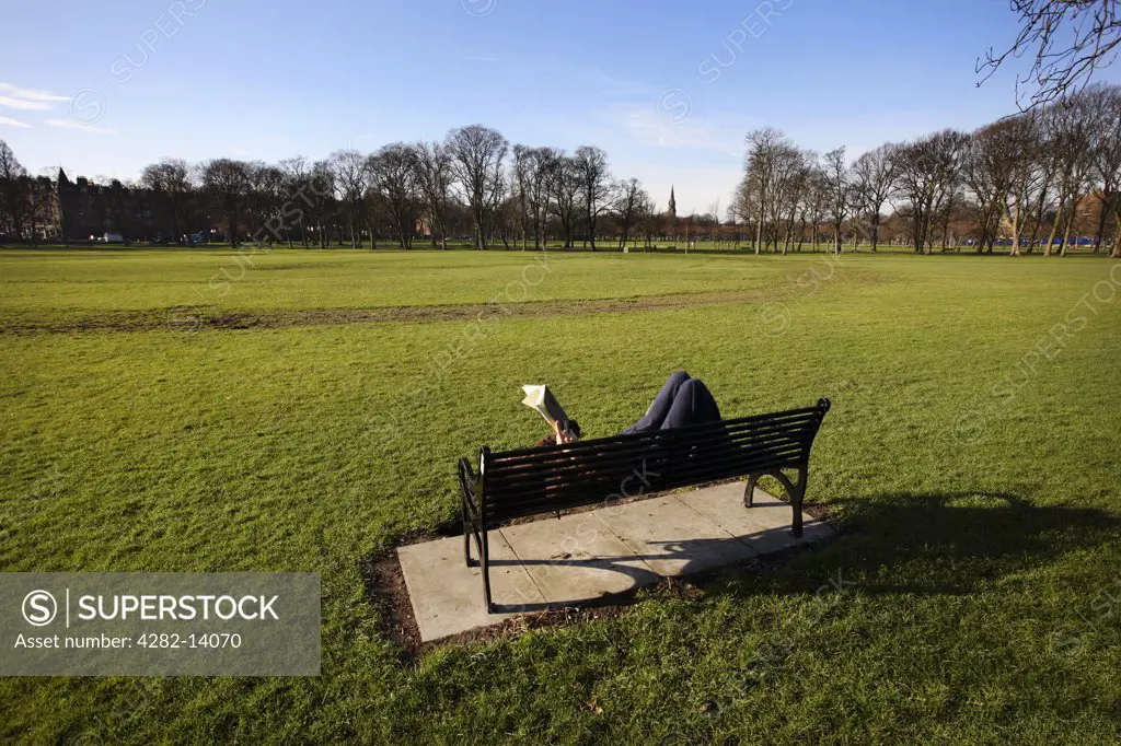 Scotland, Midlothian, Edinburgh. Man reading lying on a bench in Meadow Park in Edinburgh.