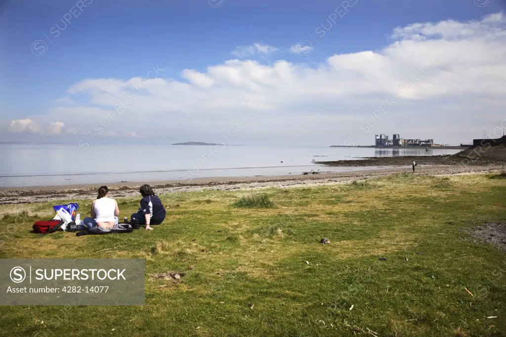 Scotland, City of Edinburgh, Edinburgh. Two people sitting on the grass looking out to sea at Granton Harbour in Edinburgh.