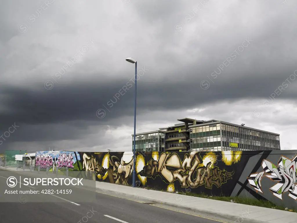 England, East Sussex, Brighton. Graffiti on hoardings in front of a sixties style building with heavy grey cloud above in Brighton.