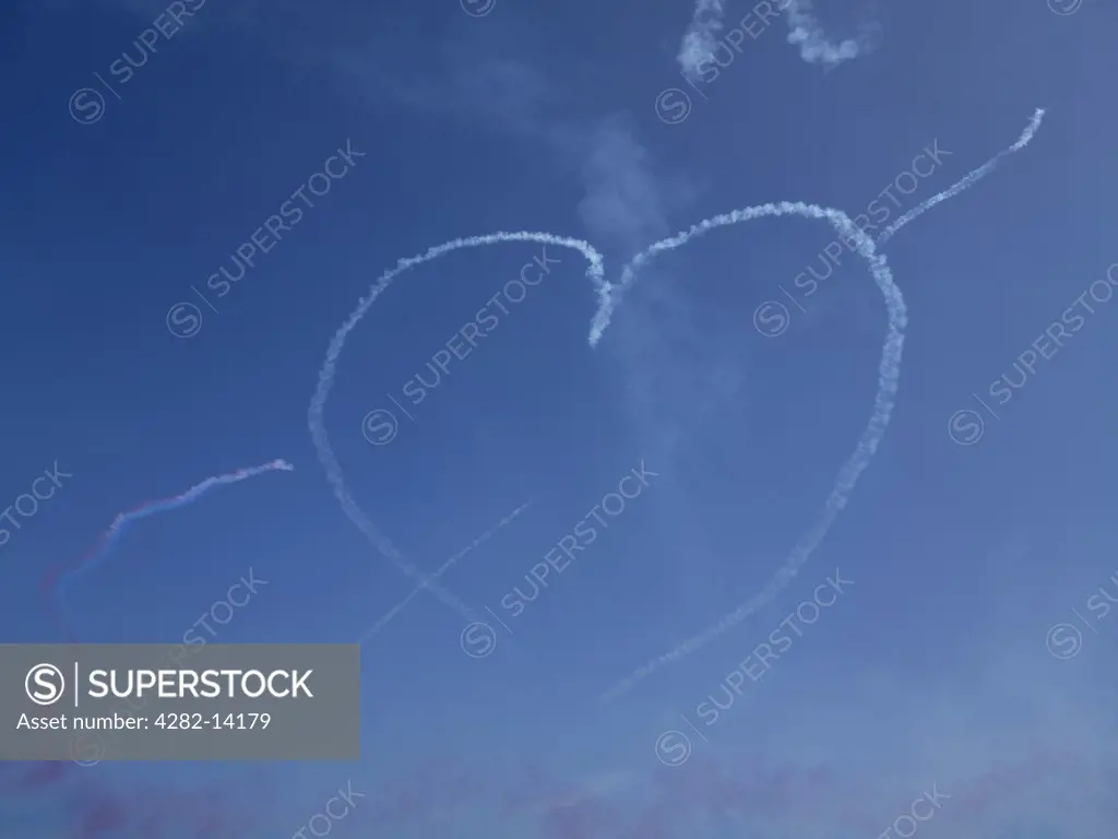 England, Channel Islands, Guernsey. A heart made of smoke hangs in a blue sky over Guernsey after a Red Arrows display.