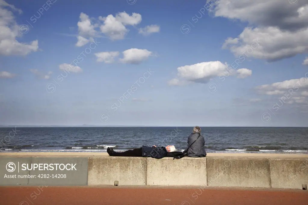 Scotland, City of Edinburgh, Edinburgh. A senior couple relaxing on the promenade of Portobello beach along the coast of the Firth of Forth.