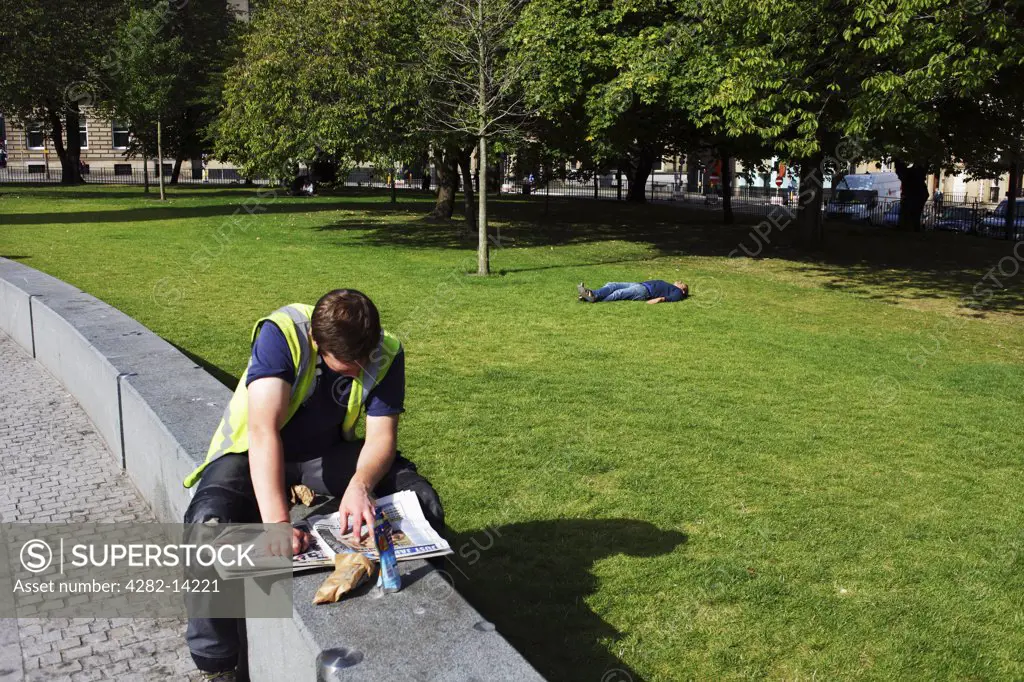 Scotland, City of Edinburgh, Edinburgh. A man taking a break from work reading a newspaper in St. Andrew Square.