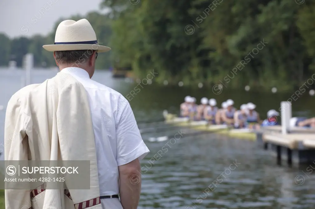 England, Oxfordshire, Henley-on-Thames. A spectator with his rowing club blazer over his shoulder standing on the riverside watching the start of a race at the annual Henley Royal Regatta.