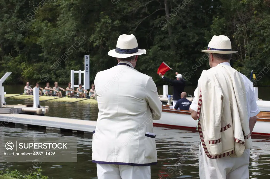 England, Oxfordshire, Henley-on-Thames. Senior rowing club members standing on the riverside watching the start of a race at the annual Henley Royal Regatta.