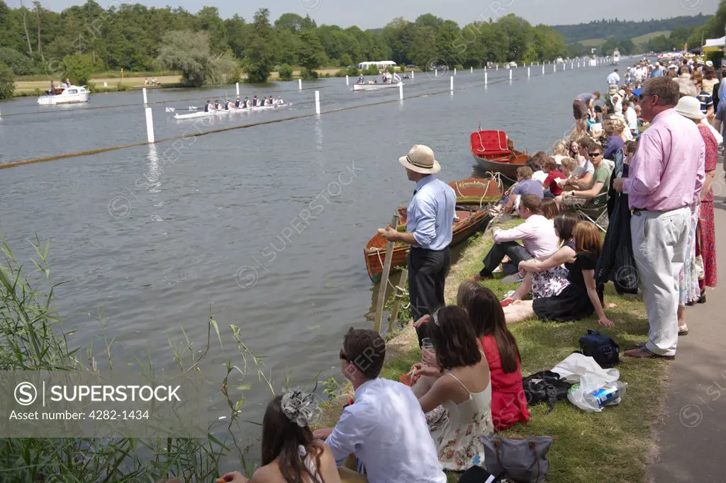 England, Oxfordshire, Henley-on-Thames. Spectators on the riverbank watching a race at the annual Henley Royal Regatta.