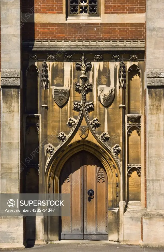 England, Cambridgeshire, Queens' College . Old ornate wooden door at Queens College in Cambridge. Queens' College is spelt with the apostrophe after the final ""s"" because the College was founded by two Queens of England.