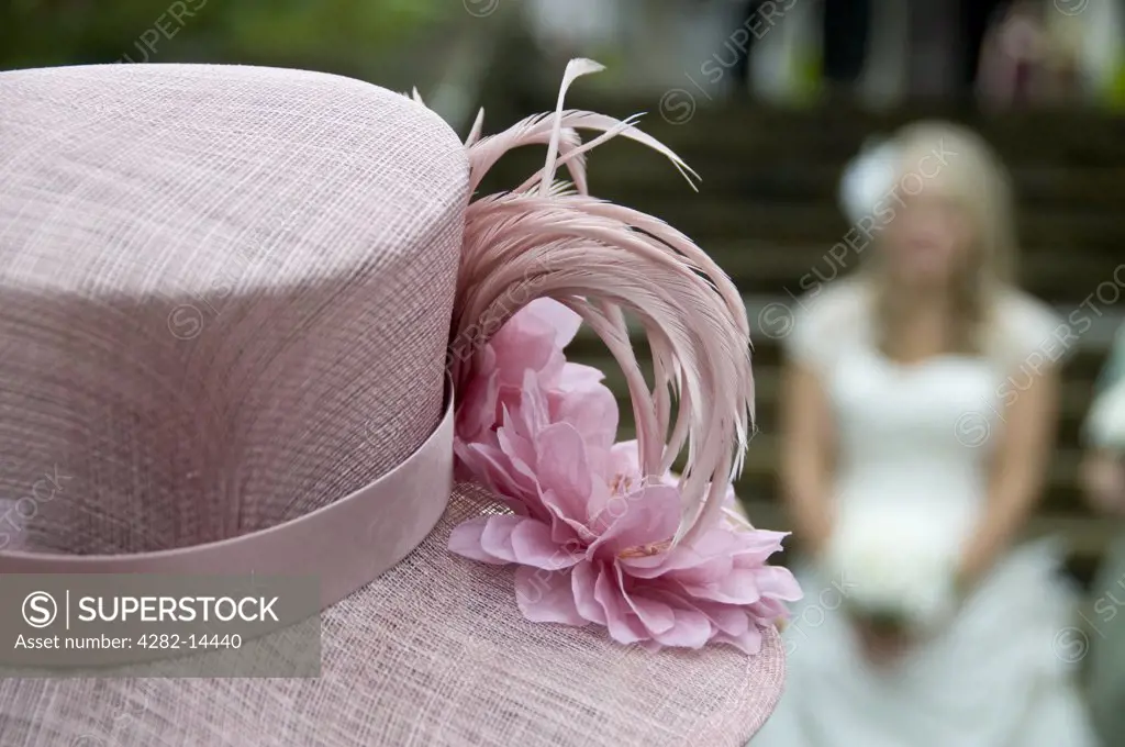 England, Lancashire, Lancaster. A close up of a pink floral hat with a blurred bride in view.