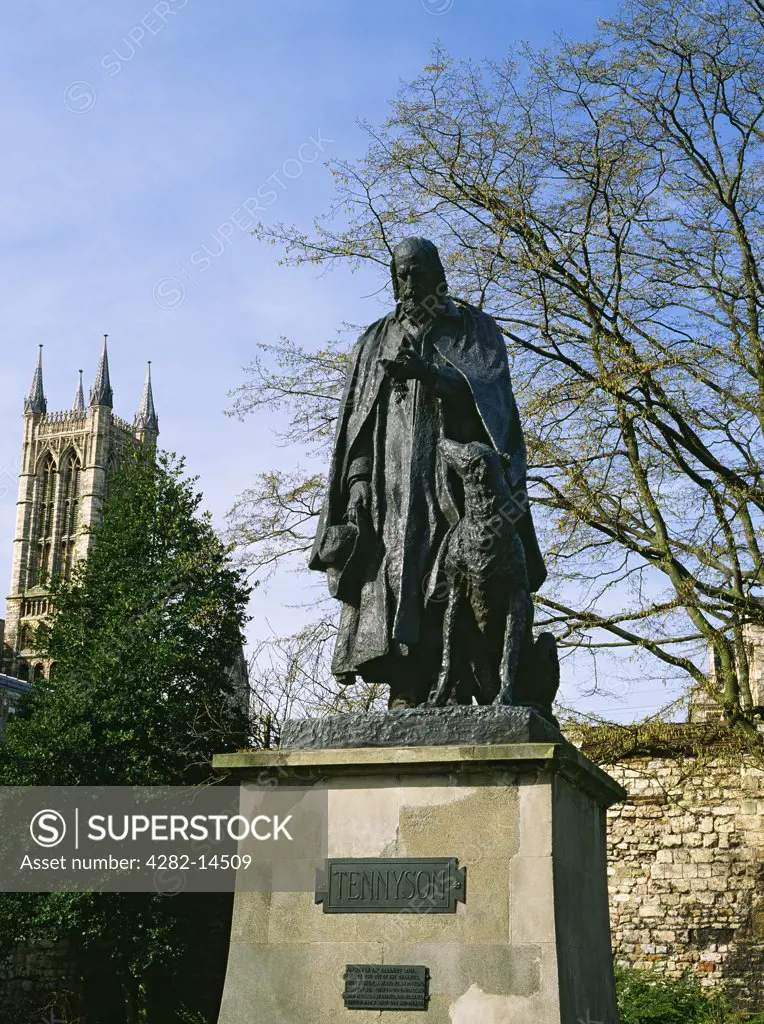 England, Lincolnshire, Lincoln. Cast bronze by George Frederick Watts of poet laureate Alfred, Lord Tennyson in Minster Yard with one of the cathedral's western towers visible to the rear.