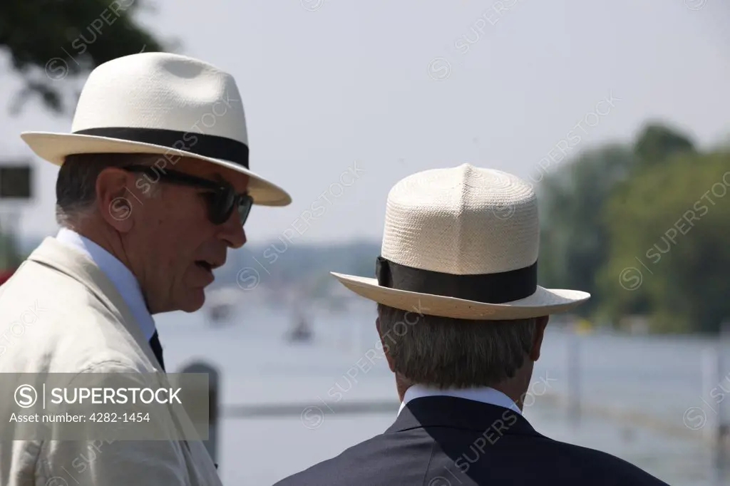 England, Oxfordshire, Henley-on-Thames. Two men wearing Panama hats spectating at the annual Henley Royal Regatta.
