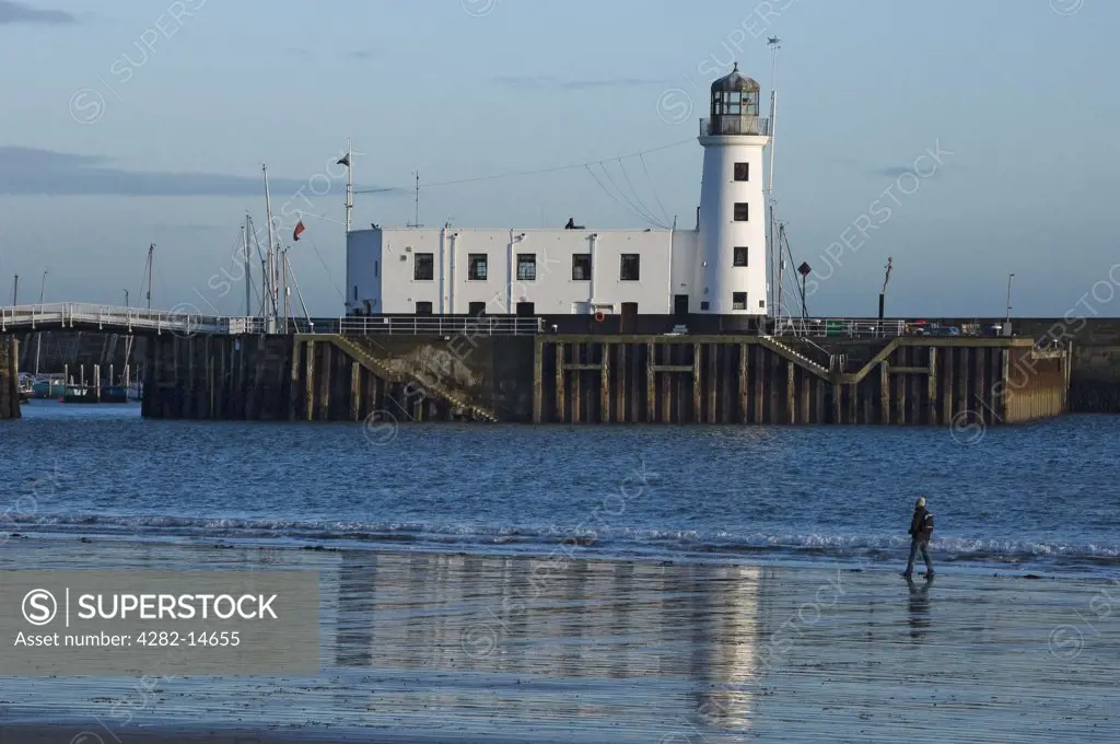 England, North Yorkshire, Scarborough. A lone person walking along the foreshore by Scarborough Lighthouse on Vincent Pier.