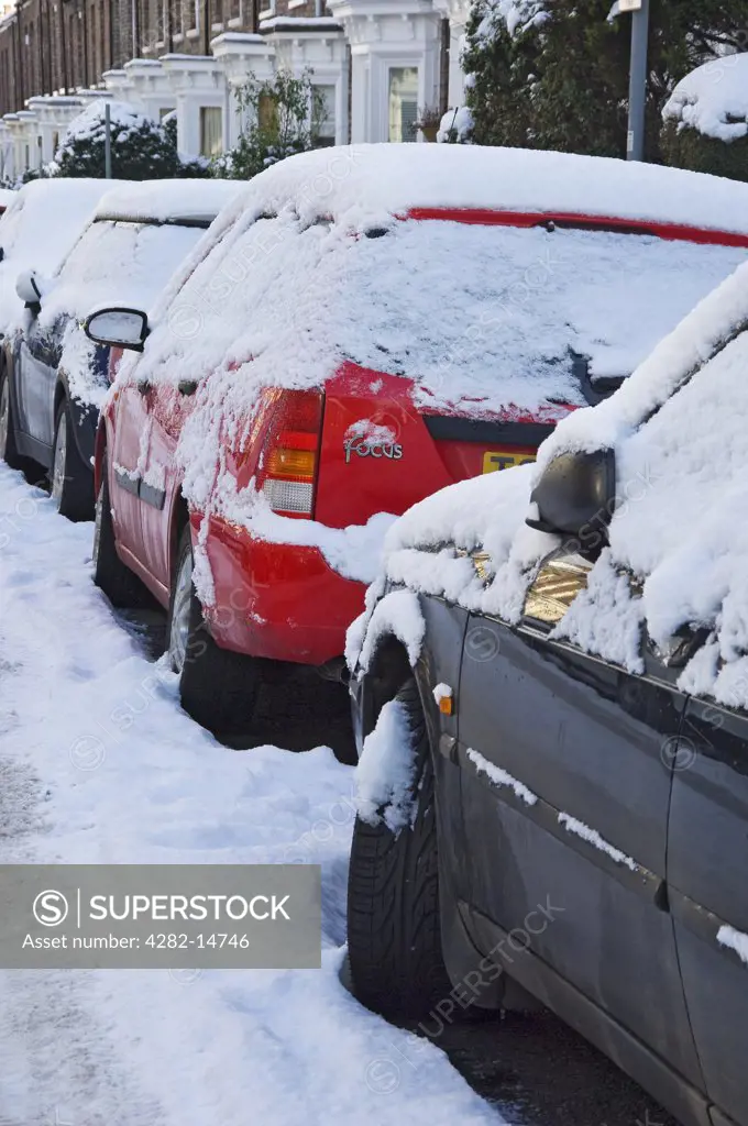 England, North Yorkshire, York. A row of snow covered cars parked along a street in York.