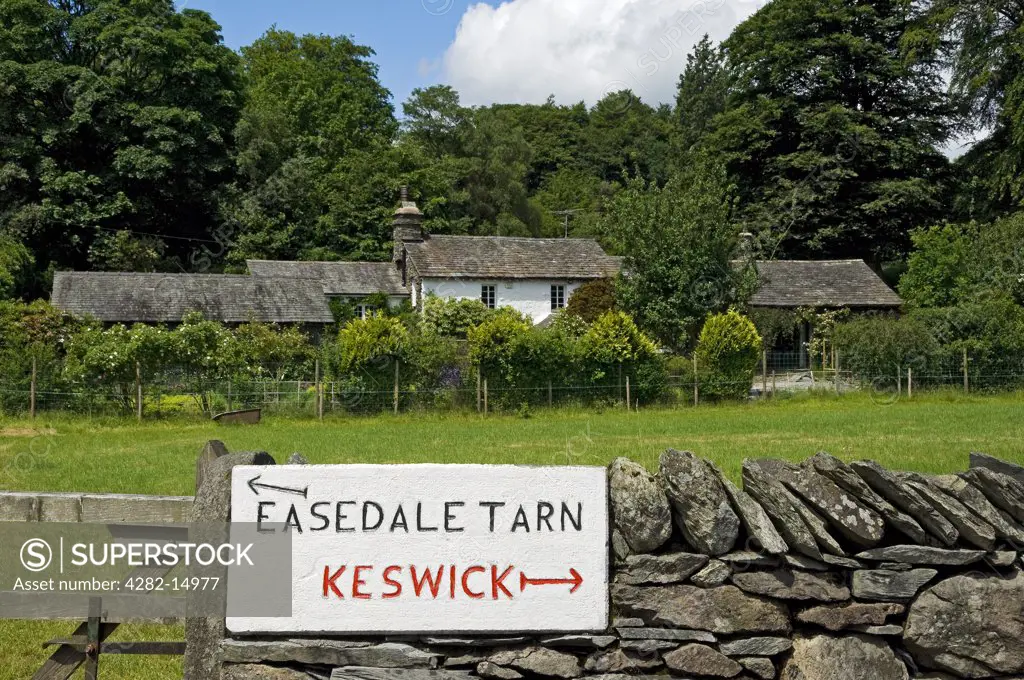 England, Cumbria, Grasmere. A hand carved sign with directions to Easedale Tarn and Keswick on a stone wall.