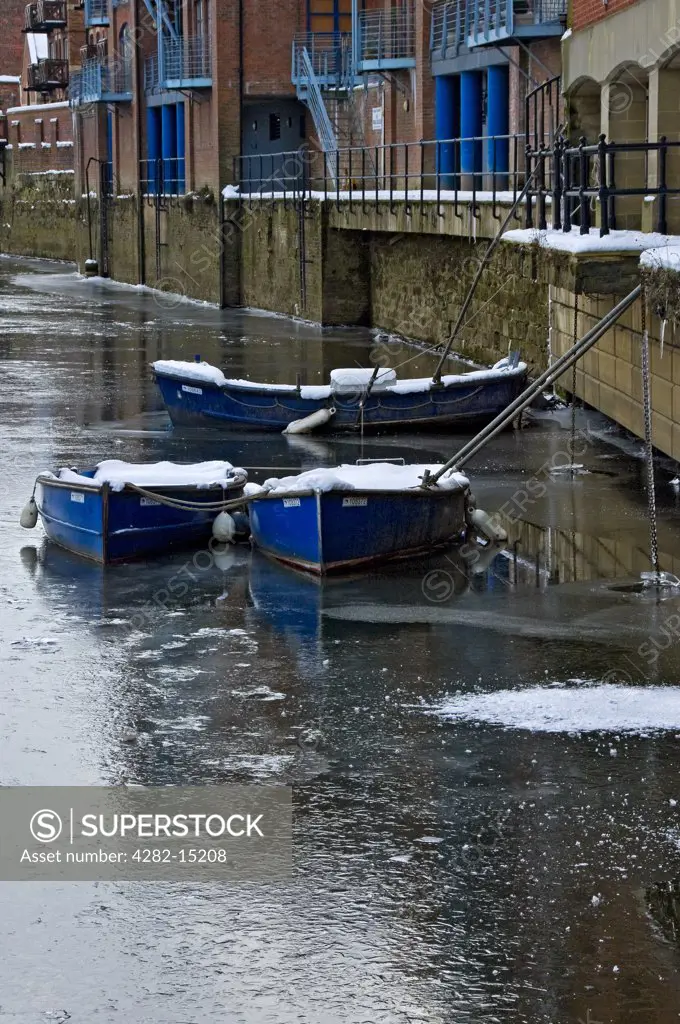 England, North Yorkshire, York. Rowing boats moored on the frozen River Ouse in winter.