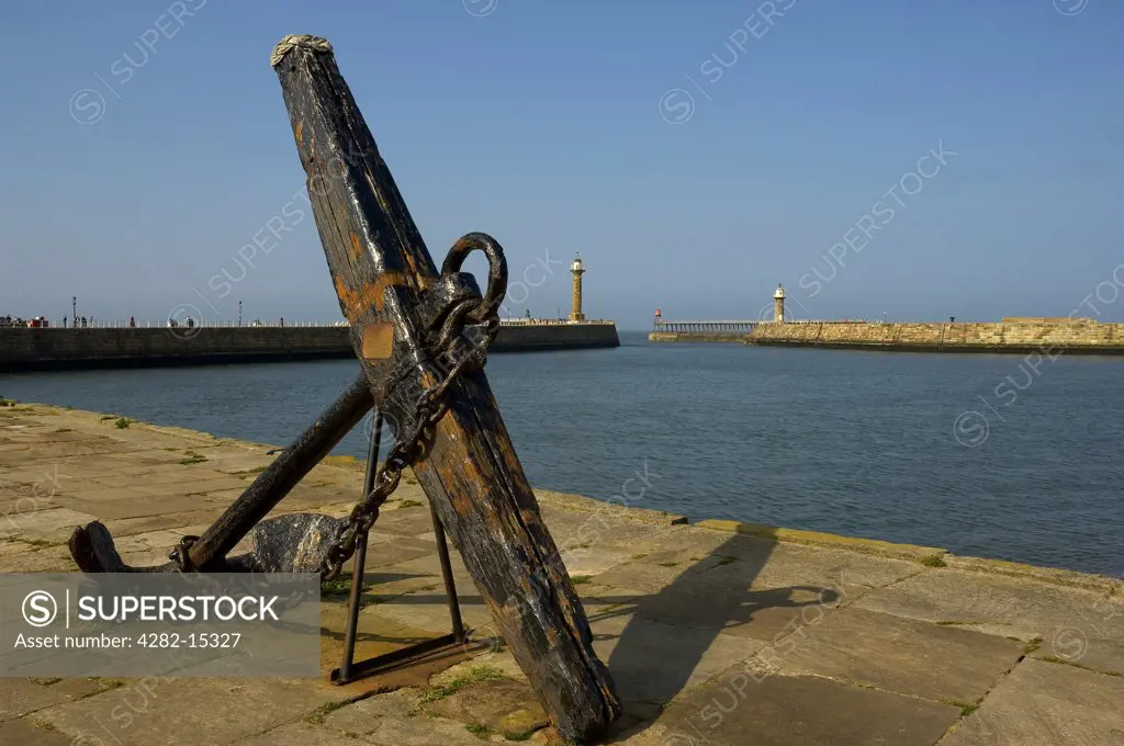 England, North Yorkshire, Whitby. An old ships anchor on the quayside with Whitby's lighthouses in the background.