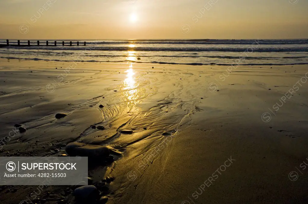 Wales, Ceredigion, Borth. Tide rolling onto the beach past a breakwater at dusk.