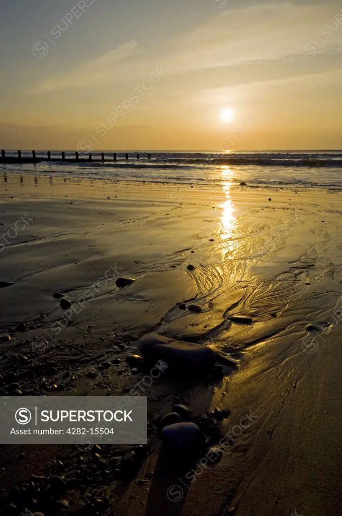 Wales, Ceredigion, Borth. Tide rolling onto the beach past a breakwater at dusk.