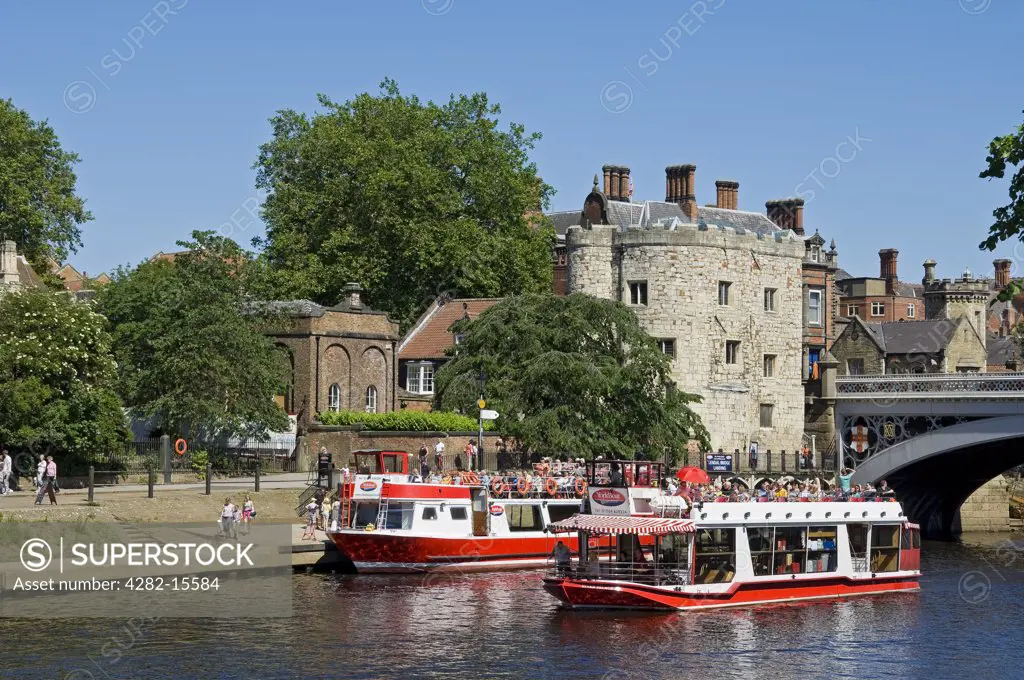England, North Yorkshire, York. Tourists aboard pleasure boats on the River Ouse at Lendal Tower.