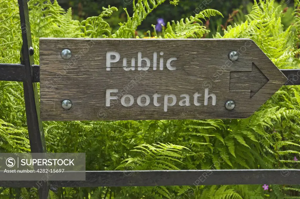 England, Cumbria, -. A wooden public footpath sign attached to a metal fence.