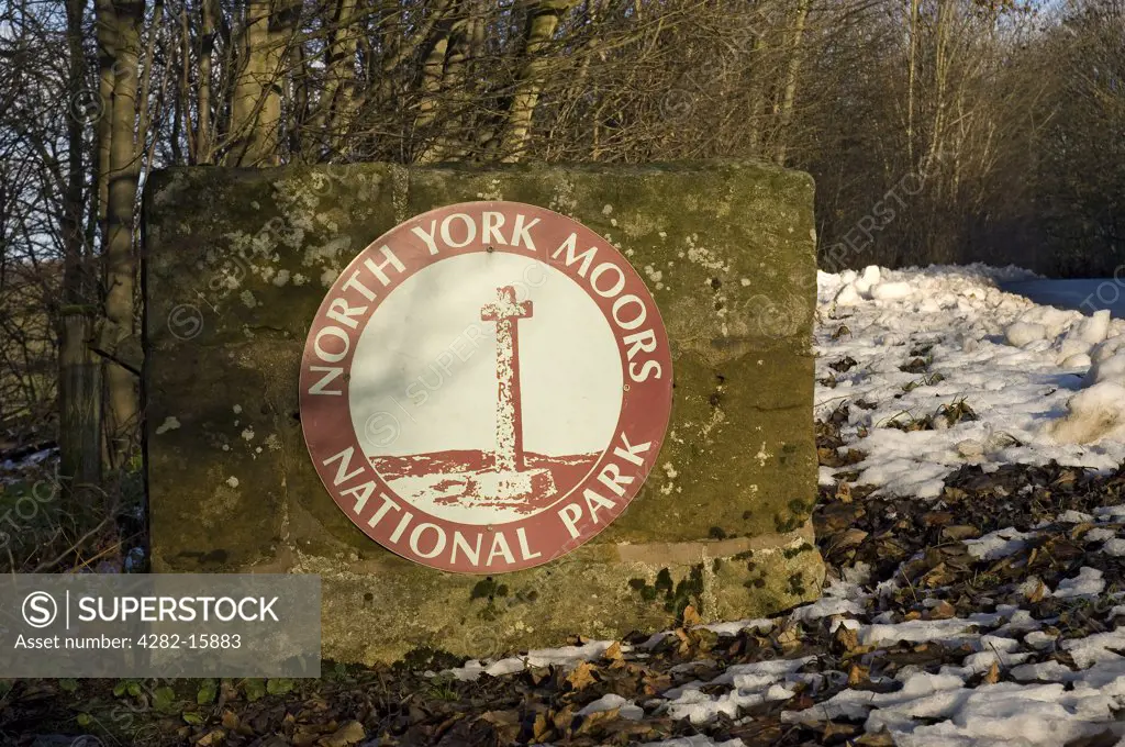 England, North Yorkshire, North York Moors. Fallen leaves and snow on the ground beside a North York Moors National Park sign.