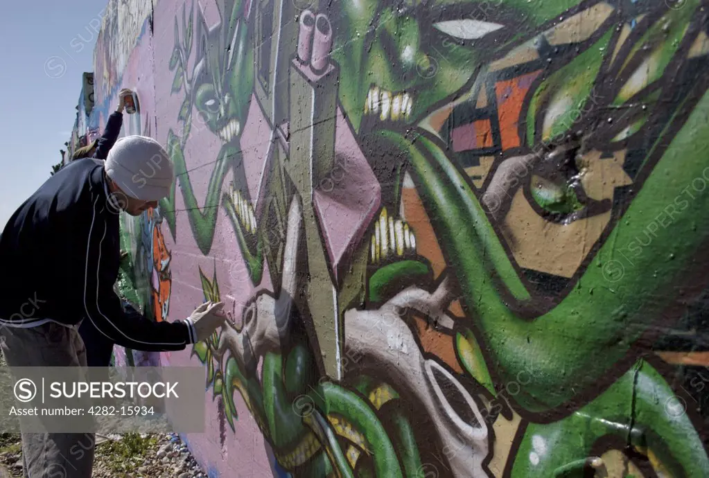 England, East Sussex, Brighton. A graffiti artist at work. The word 'graffiti' is the plural of 'graffito' and originates from the Italian word 'graffiato' which means scratched.