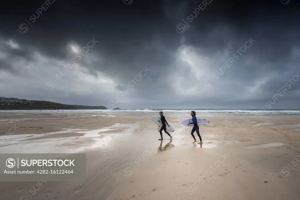 Surfers walking on Fistral Beach as dark gloomy storm clouds approach Newquay in Cornwall.