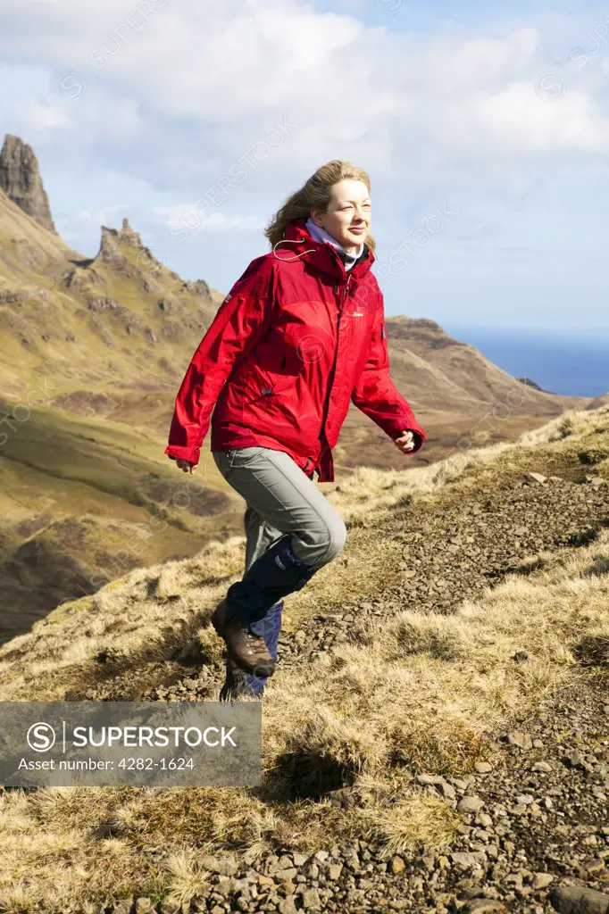 Scotland, Isle of Skye, Trotternish. A female walker wearing a red waterproof climbing up a path over the Quiraing.
