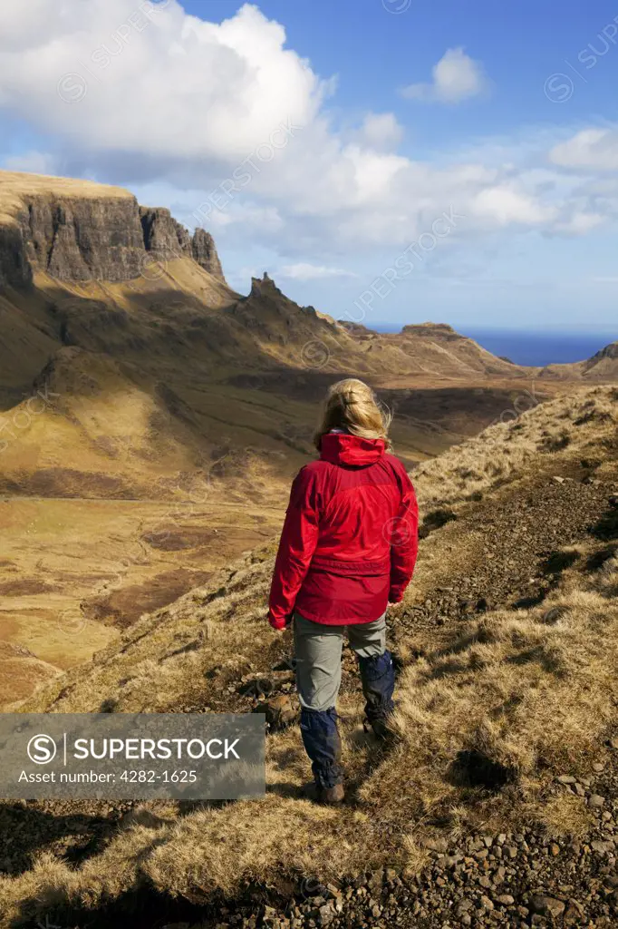 Scotland, Isle of Skye, Trotternish. A female walker wearing a red waterproof looking out at the stunning landscape on the Trotternish Peninsula from the Quiraing.
