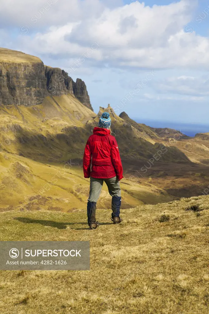 Scotland, Isle of Skye, Trotternish. A female walker wearing a red waterproof looking out at the stunning landscape on the Trotternish Peninsula from the Quiraing.