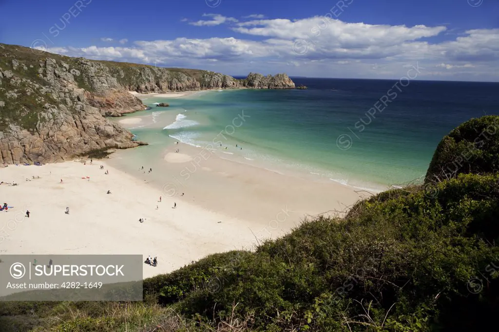 England, Cornwall, Porthcurno. People enjoying the sunshine on Porthcurno beach with Logan Rock in the distance. The beach and bay are regarded as one of the ten most beautiful bays in the world.