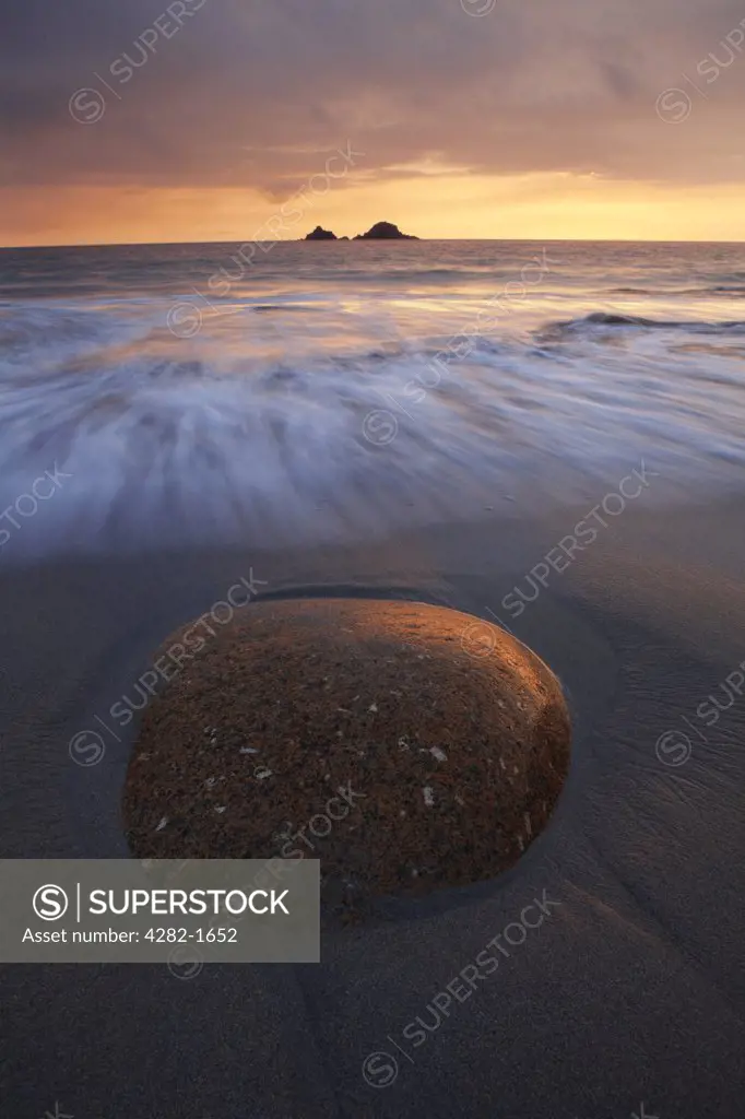 England, Cornwall, Porth Nanven. The tide rolling onto Porth Nanven beach towards a large ovoid rock in the foreground at sunset.