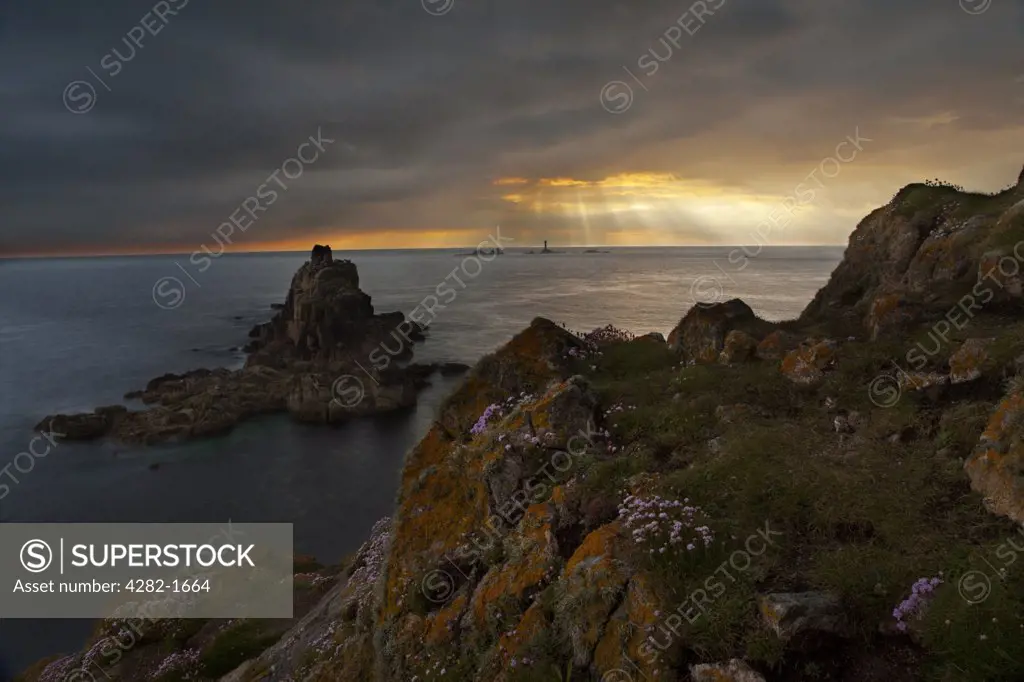 England, Cornwall, Land's End. Rays of sunlight breaking through storm clouds over Longships Lighthouse, viewed from Land's End at sunset.